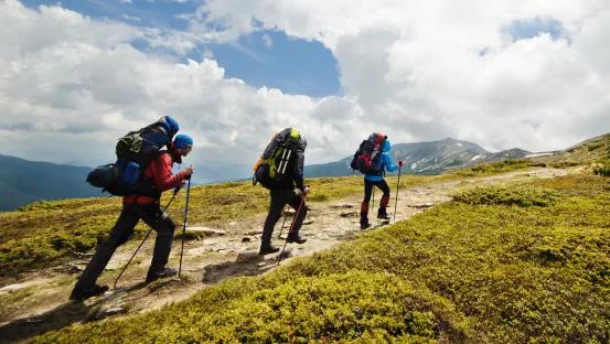 a group of people with backpacks walking along the road there are mountains on the horizon